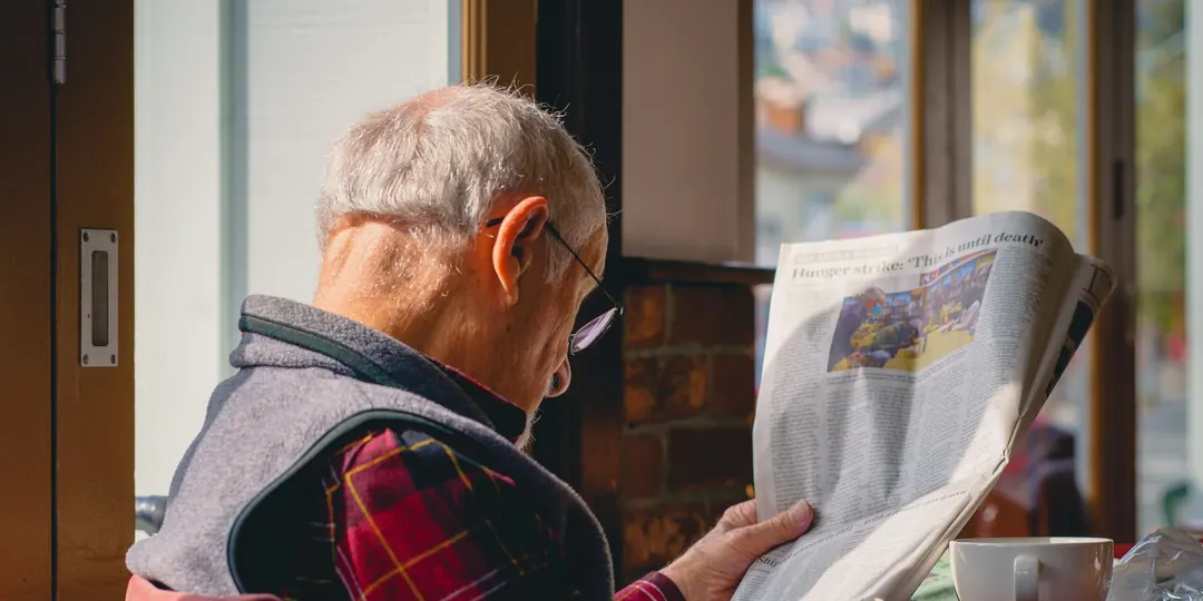 A man reading the newspaper over a cup of coffee