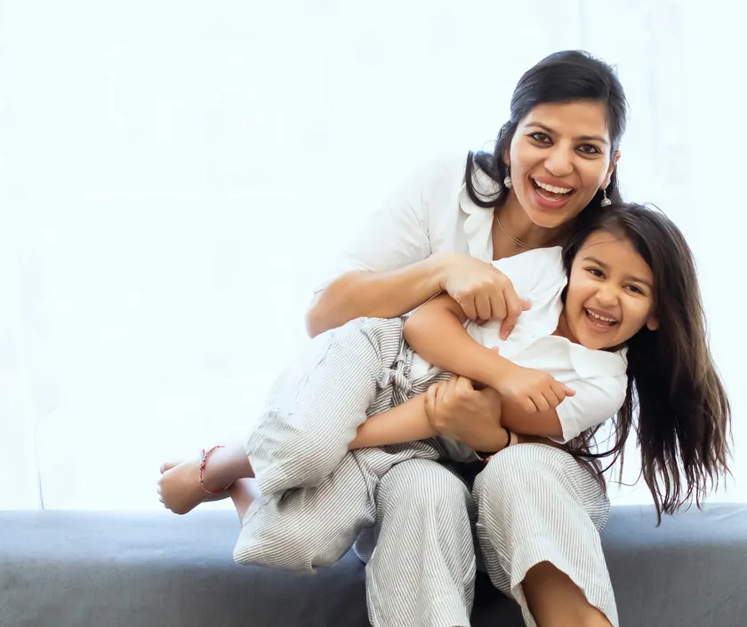 A mother holding her laughing daughter on the sofa