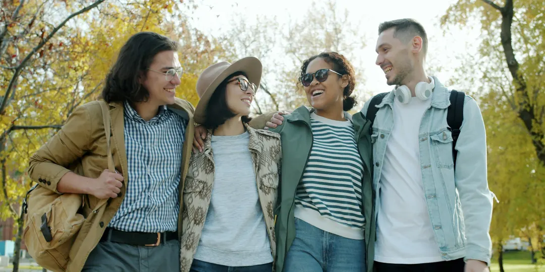 Four friends walking and laughing together in the park